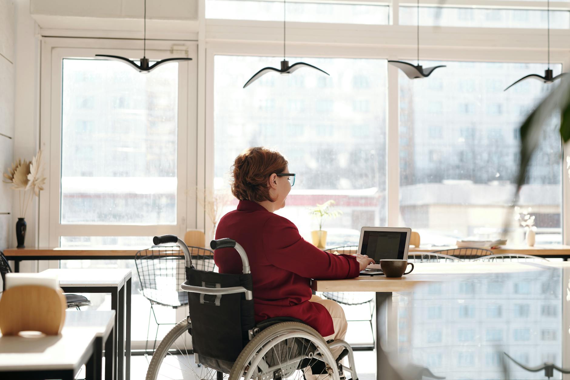 Kobieta na wózku inwalidzkim pracuje zdalnie przy laptopie w kawiarni