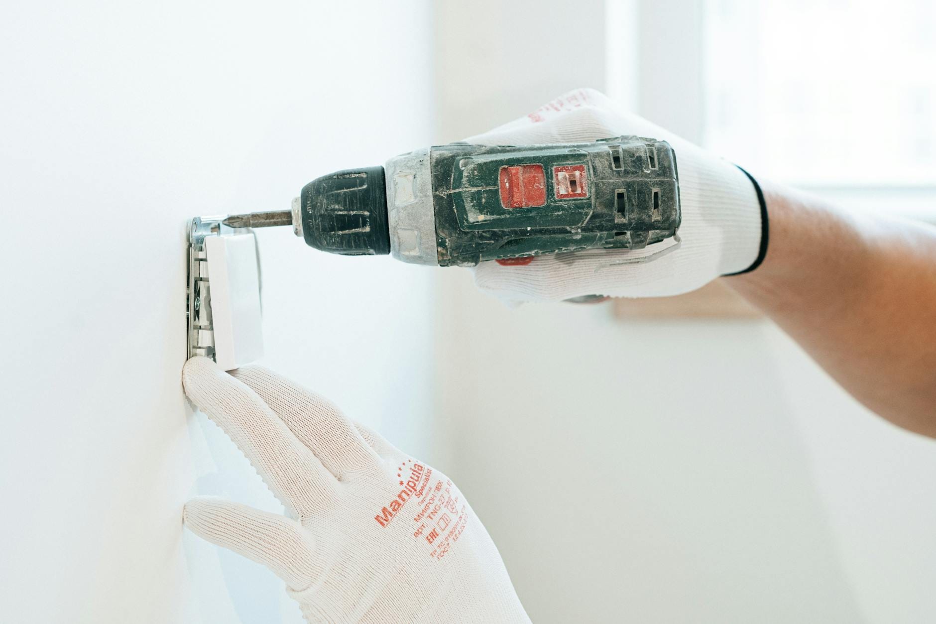 Elektryk w rękawicach montuje gniazdko w ścianie w bezpieczny sposób