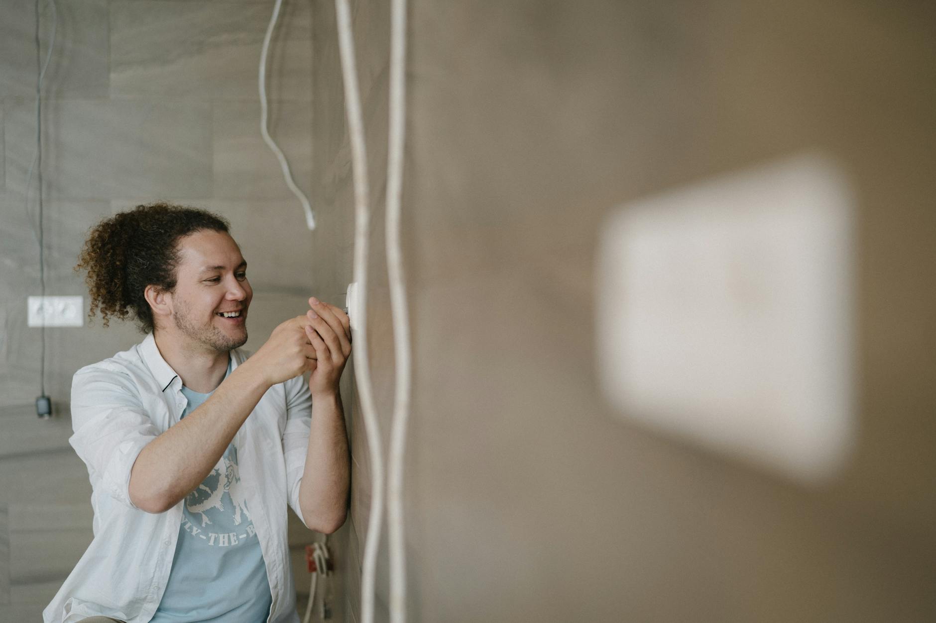 Elektryk z kręconymi włosami uśmiechnięty przy montażu gniazdka