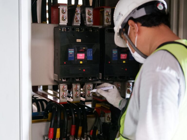 Technik w odzieży ochronnej sprawdza rozdzielnice elektryczne w hali przemysłowe